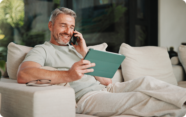 Image shows a man looking at a tablet while on the phone